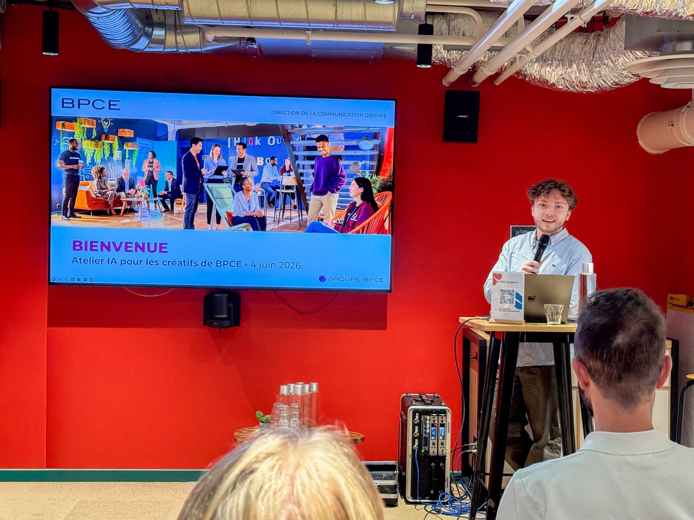 Victor at the lectern, mic in hand, next to the screen "Bienvenue, Atelier IA pour les créatifs de BPCE, 4 juin 2026" (Welcome, AI workshop for BPCE's creatives, 4 June 2026).