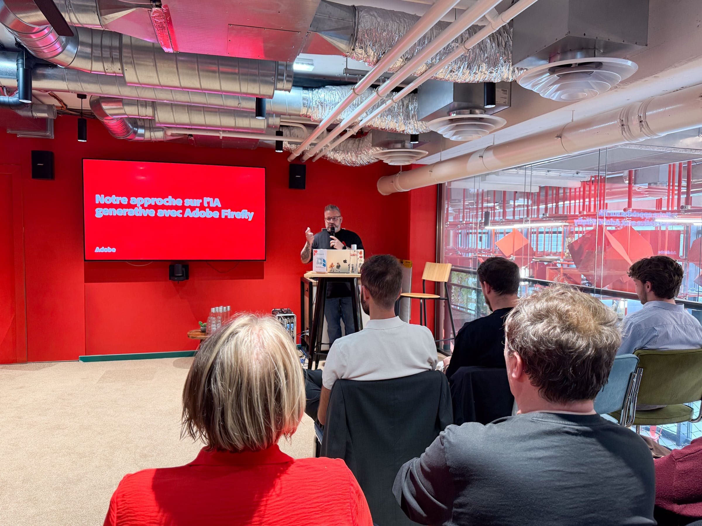 A speaker at the lectern in front of the slide "Our approach to generative AI with Adobe Firefly", facing the audience.