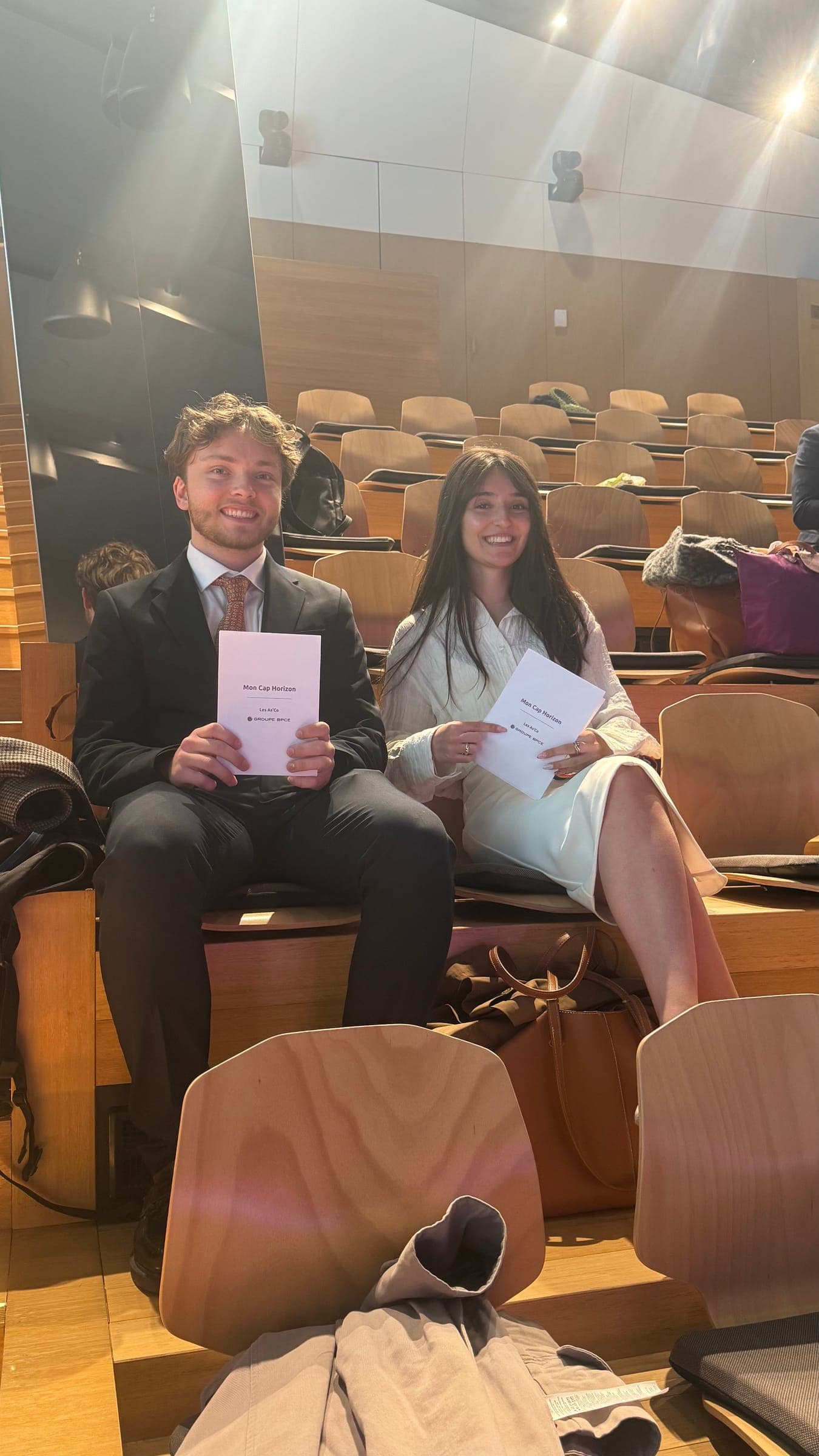 Victor and Cindy Alves sitting side by side in the lecture hall, smiling, each holding the Mon Cap Horizon booklet.