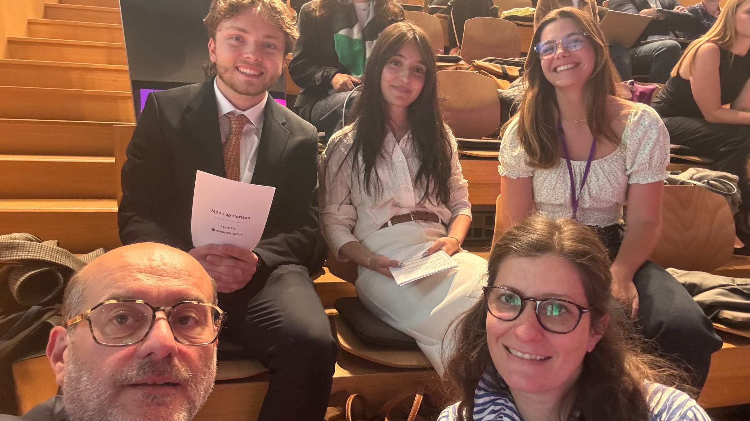 Group selfie in the lecture hall: Victor and Cindy Alves hold the Mon Cap Horizon booklet, surrounded by three other people.